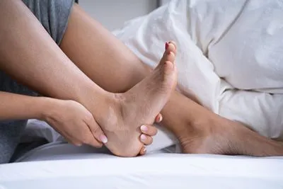 Person-holding-ankle-in-bed