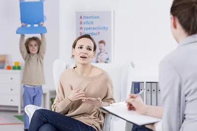 Pediatric visit showing mom discussing concerns as energetic child plays behind