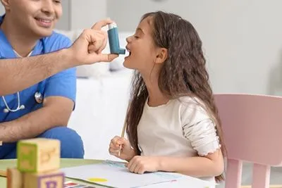 Child learning how to use an asthma inhaler with pediatrician's help