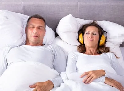 Woman covering ears with headphones while man snores