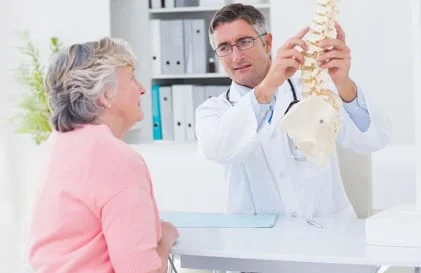Chiropractor pointing to model spine with patient