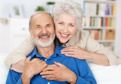 older woman embracing older man sitting on couch, both smiling nice dentures Kearney, NE dentist