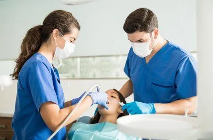 female dentist and male assistant do dental work in woman's mouth, dentist North York, ON