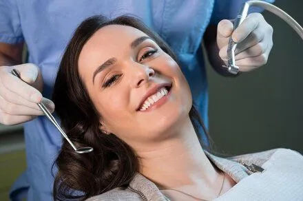woman smiling, dentist behind her holding dental tools, dentist Frederick, MD general dentistry