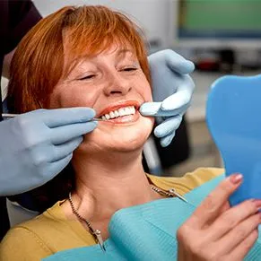 red haired woman looking in mirror at dental work, cosmetic and general dentist Honolulu, HI