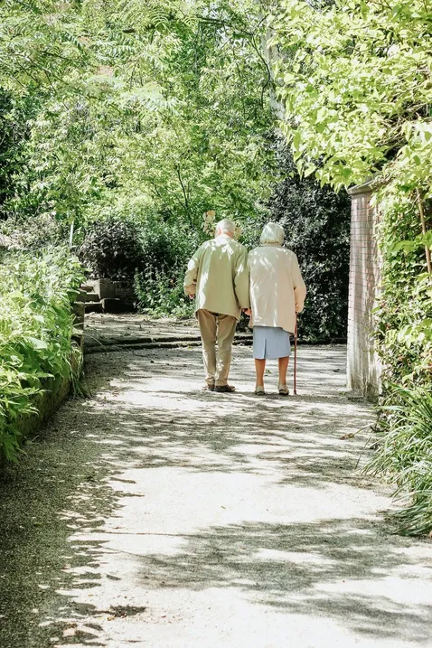 senior couple taking a walk on a path under lots of green trees on a sunny day