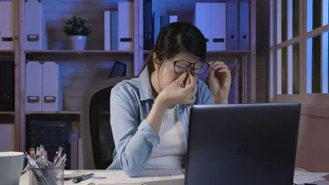 Female rubbing eyes in front of computer