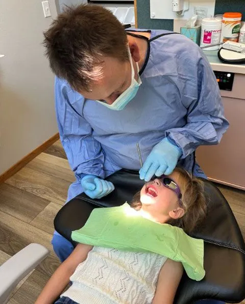 Dr. Igor Sitnik DMD performing dental exam on little girl lying back in dental chair, dentist Salem, OR