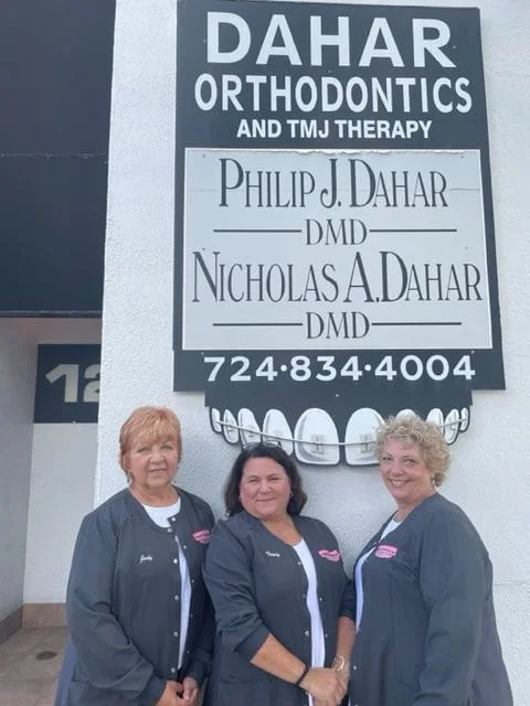 Three staff outside in front of office sign