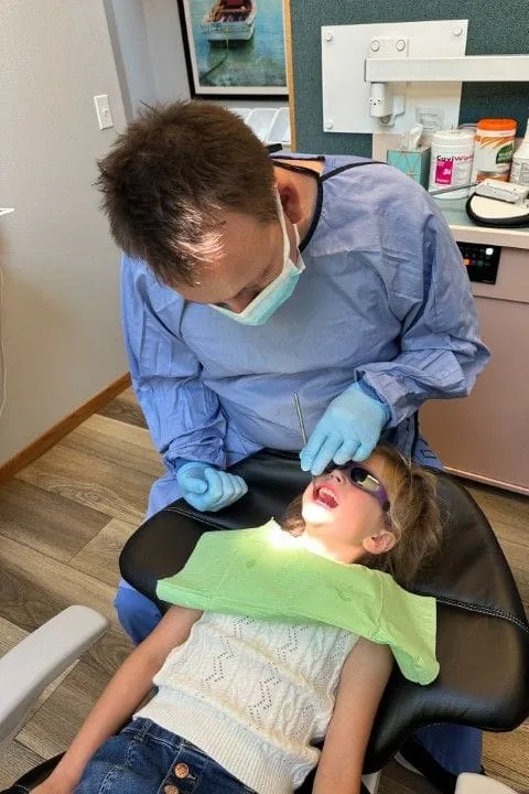 Dr. Igor Sitnik DMD performing dental exam on little girl lying back in dental chair, dentist Salem, OR