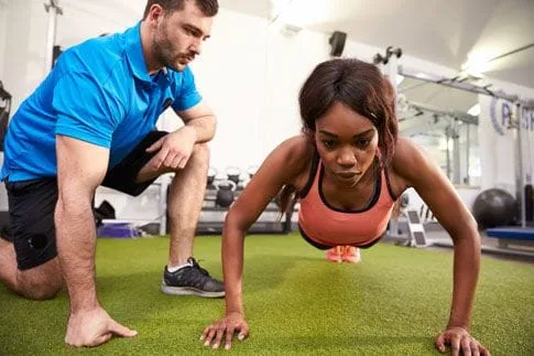 A man, possibly a coach, kneeling next to a woman doing pushups.