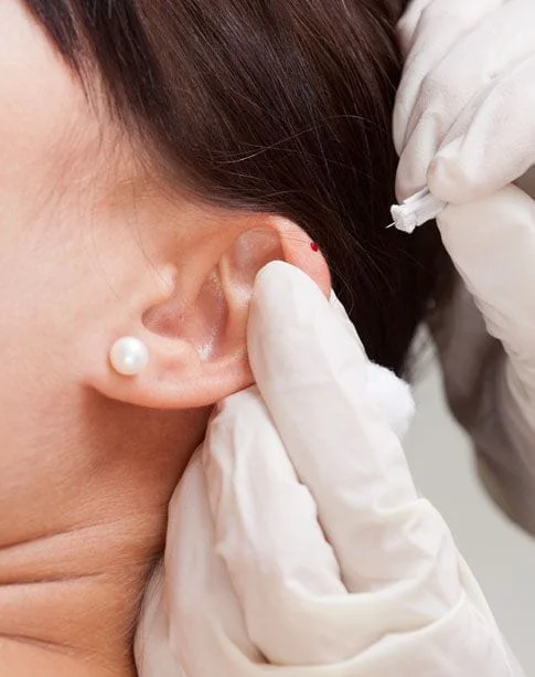 Ear with a dot of blood from needle