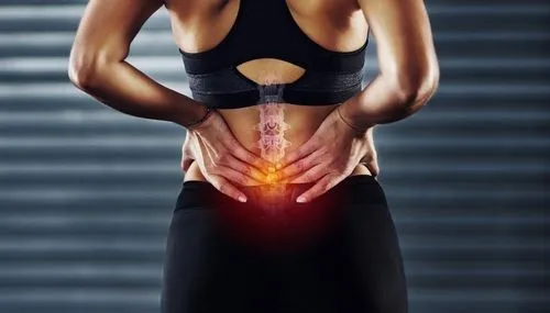 Woman holding her lower back in pain with a spine anatomy overlay highlighting the painful area.