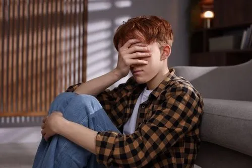 Teen showing signs of depression, face in hand while thinking about mistakes.