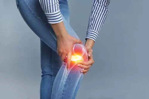 Woman holding knee due to pain on gray background