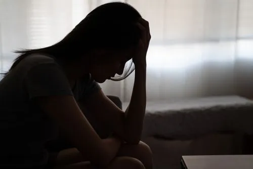 Depressed woman with hands on head, sitting in the dark, worried and sad