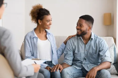 Happy couple looking at each other while attending relationship counseling with therapist.