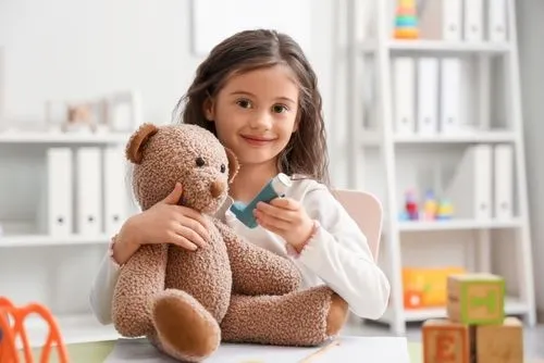 Child holding a teddy bear and an asthma inhaler for respiratory care.