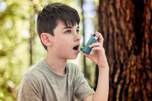 Child outdoors using an inhaler to prevent an asthma attack