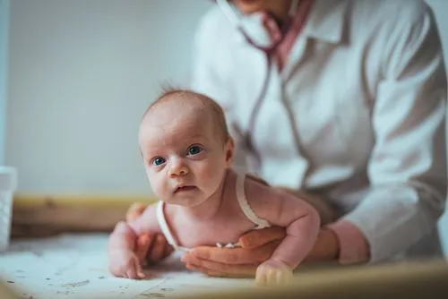 Newborn baby being examined during a pediatric check-up with the doctor in the background