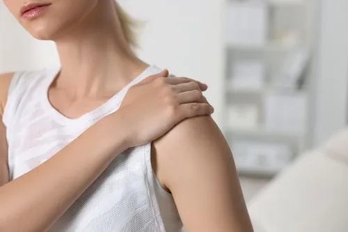 A woman holding her shoulder in discomfort while at home.