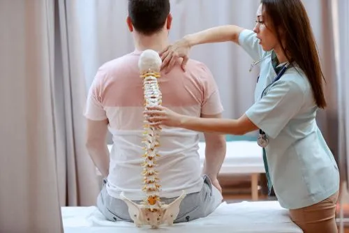 A chiropractor holding a spine model over a patient's back to explain spinal care.