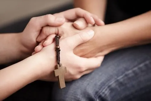 Two people holding hands with cross in prayer