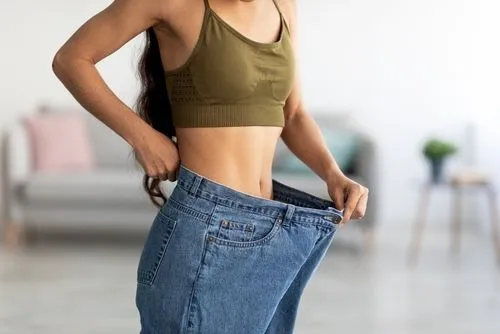 Woman showing weight loss progress by fitting into her old jeans