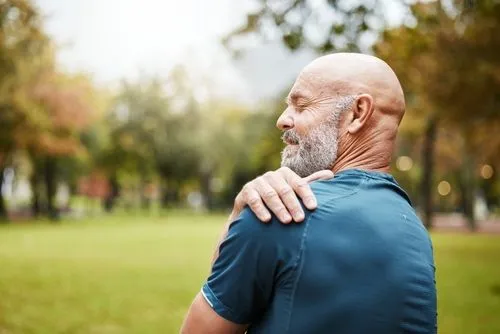 Elderly man outdoors holding his shoulder in pain.