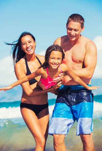 family on a beach, parents holding young girl in air laughing, family dentistry Hilo, HI dentist