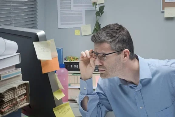 A man with glasses having hard time looking at a computer