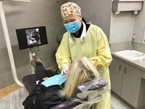 female dental assistant examining female patient, X-ray on screen in background, Invisalign Millbrae, CA dentist