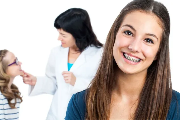 girl with braces smiling, orthodontist in background with patient. Frederick, MD orthodontics