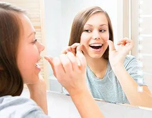 girl looking in bathroom mirror flossing teeth, general dentistry Kanata, ON dentist