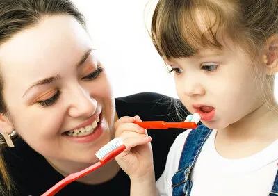 woman holding toothbrush showing toddler girl how to brush teeth, pediatric dentistry Little Falls, NJ dentist