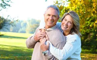 older white man and woman hugging and smiling, outside in park near trees, cosmetic dentures San Diego, CA, dentist downtown San Diego