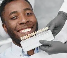 black man smiling, dentist holding tooth shade samples by his mouth, cosmetic dentistry Melrose, MA dentist