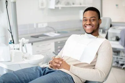 young black man smiling wearing dental bib sitting in dental exam room, dentist Brookline, MA