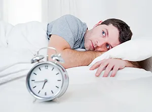 man lying awake in bed next to alarm clock, treatment for sleep apnea Montclair, NJ dentist