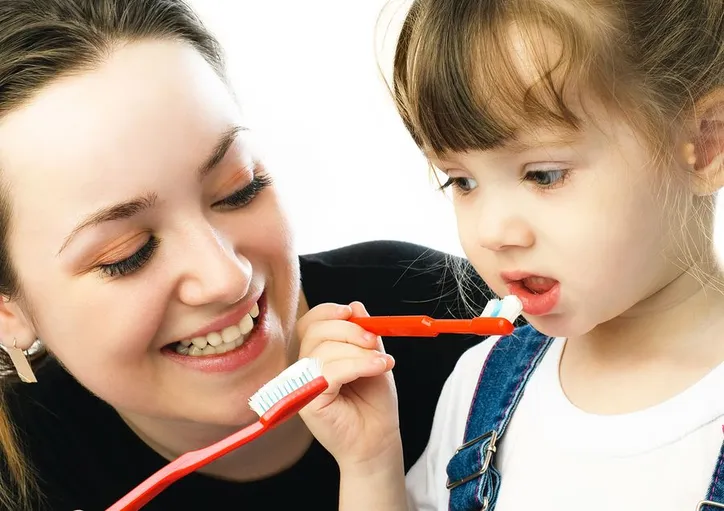 mom showing toddler daughter how to use toothbrush, children's dentistry Durham, NC family dentist