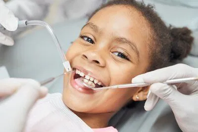 young black girl lying back in dental chair smiling, dental tools near mouth, pediatric children's dentist North York, ON