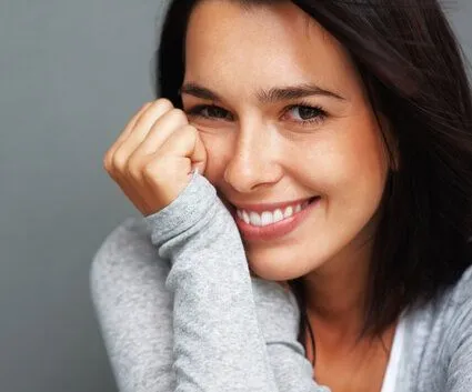 dark haired woman smiling leaning her head on her hand, dental bridge Philadelphia, PA general dentist