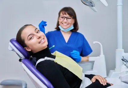 teen girl wearing dental bib sitting in exam chair, dental hygienist performing dental cleaning, Brookline, MA dentist