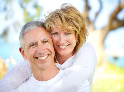 older woman hugging older man outdoors near trees and lake, both smiling with nice teeth, dentures Harrisburg, PA