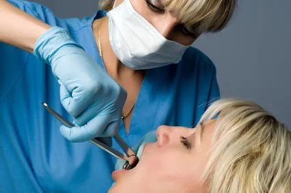 female periodontist using tool to extract tooth from woman's mouth, tooth extractions Albuquerque periodontal surgery 