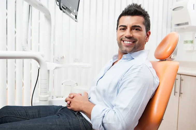 man smiling sitting in orange dental exam chair, getting dental implants Longmont CO dentist