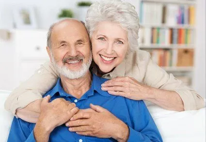 older woman smiling embracing older man sitting on couch, nice dentures North York, ON dentist