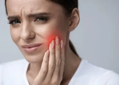 woman holding jaw in pain and wincing, red area on face indicating pain, emergency dental care Detroit, MI emergency dentist