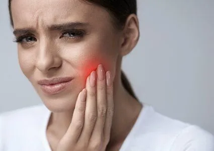 woman wincing and holding jaw in pain, red spot on face indicating pain, emergency dental care North York, ON dentist