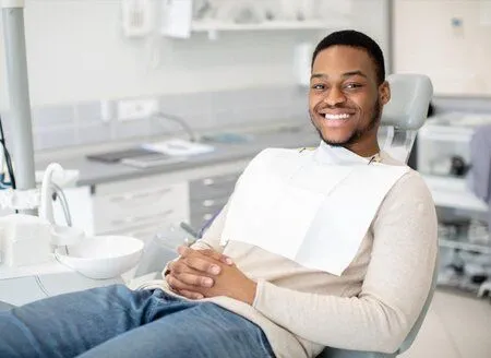 young black man smiling, sitting in dental exam chair wearing dental bib, dentist Montclair, NJ general dentistry
